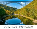 New River Gorge Bridge scenic view in fall. View from the lower gorge with reflection of the bridge in the river and fall foliage on the mountain sides.  Horizontal color photo. 