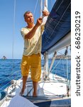 Small photo of Adult man working on sailboat, tying a knot on the the ropes on sails of the yacht, sailor yachtsman controlling the sail on sailing boat. Yachting sport activities and sailing