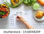 Calories control, meal plan, food diet and weight loss concept. top view of hand filling meal plan on weekly table with salad and fresh vegetable on dining table