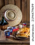 Small photo of Chilean independence day concept. fiestas patrias. Tipical baked empanadas de pino, wine or chicha, hat and play emboque. Dish and drink on 18 September party, wooden background.