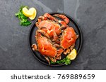 Cooked crabs on black plate served with white wine, black slate background, top view.