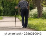 Small photo of frail man walking with difficulty with walking sticks