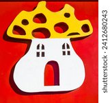 Small photo of The adorable image features a wooden mushroom cut by fretwork, painted in yellow and white, placed on a vibrant red background. A playful and educational object, perfect for stimulating the creativity