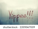 Small photo of Yippee Handwritten lettering exclamation on misted glass on blue window with raindrops