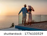 A romantic couple with hats on vacation time enjoys the summer sunset by the pool
