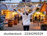 A happy tourist woman stands on a christmas market in Copenhagen, Denmark, with illuminated decorations during winter dusk