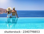 A couple hugging at the edge of an infinity pool and enjoying the view to the blue, mediterranean sea during summer vacation time
