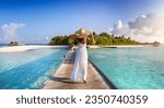 Small photo of Back view of a elegant woman in white dress and hat walks down a pier towards a tropical island in the Maldives
