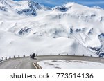 Austria, Tyrol, High Alpine road. Snowy scenery. Family traveling by motorcycle, moving on speed by road curve of Grossglockner Hochalpenstrasse at snowy Alps mountains background. Sunny May day.