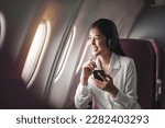 Cheerful female passenger in headphones for noise cancellation watching online movie during intercontinental flight in cabin of aircraft, happy young woman using wifi connection on board