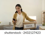 Small photo of Donation concept. Woman asian holding a donate box with full of clothes. Woman holding clothes donate box. Clothes in box for concept donation and reuse recycle