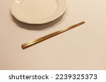 A set of Korean brass chopsticks with empty white dish on the table, the chopstick on the dish