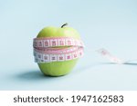 Apple with measuring tape on blue background. Weight loss, counting calories and healthy eating concept - calculate daily nutrition intake. Copy space.