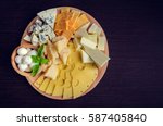 Cheese plate: Parmesan, cheddar, gouda, mozzarella and other with basil on wooden board on dark background with place for text. Tasty appetizers. Top view. Copy space.