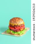 Small photo of Homemade double burger minimalist on a green colored background. Vertical image with a juicy and delicious cheeseburger packed up with wax paper.