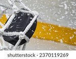 Small photo of A close-up view of an Ice Hockey puck hitting the back of the goal net as shavings fly by, viewed from the side. Scoring a goal in ice hockey.