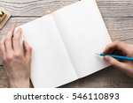 young woman hands hold opened notebook pages with blue pencil in light wooden table with bookmarks
