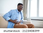 Small photo of Young African man holding his stomach in pain, Man with reflux disease holding his belly with painful expression