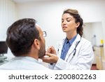 Small photo of Male patient opening his mouth for the doctor to look at his throat. Female doctor examining sore throat of patient in clinic. Otolaryngologist examines sore throat of patient.