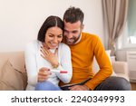 Small photo of Joyful couple finding out results of a pregnancy test at home. Happy couple looking at pregnancy test. Woman surprising her husband with positive pregnancy test, he seems reasonably pleased