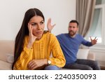 Small photo of Young couple having argument - conflict, bad relationships. Angry fury woman. Angry young couple sit on couch in living room having family fight or quarrel suffer from misunderstanding