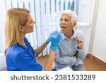 Small photo of Senior patient opening her mouth for the doctor to look in her throat. Female doctor examining sore throat of patient in clinic. Otolaryngologist examines sore throat of patient.