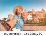 Happy asian girl traveller taking selfie photo with the famous luxury Atlantis hotel building on a Jumeirah Palm Island in Dubai, UAE. Vacation and tourist destination concept