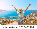 Happy woman with open arms stands on the viewpoint and enjoys the panorama of Kas resort town of the Mediterranean sea in Turkey
