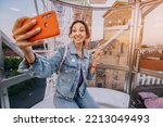 A traveler girl takes a selfie photo for social networks at an amusement fair inside a Ferris wheel booth on the old European city square