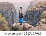 Man standing on his head on the edge of a big cliff with view of canyon Tazi in Turkey. Yoga pose concept