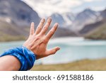 The hand is trying to reach moutain lake, travel concept
