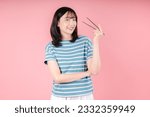 Image of young Asian woman holding chopstick on pink background