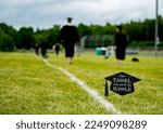 Small photo of High school seniors walk across football field at graduation. In the foreground is a sign with a mortarboard that reads the tassel was worth the hassle.