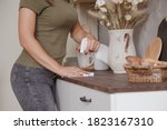 Small photo of Young woman without gloves cleaning table with spray rag in kitchen