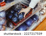 Woman's hand chooses blue glass Christmas ball decoration for a Christmas tree in the store. Color of New Year. Preparation for winter holidays