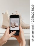 Small photo of A woman takes a picture of new shoes on a mobile phone at home. Mobile shooting for goods for sale. Blogger and stylist photographing clothes. Reusing unnecessary things