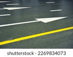 Wet asphalt road with yellow lines and white arrows.