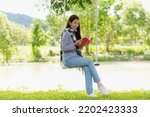 Lifestyle people girl reading book and drinking coffee for education outdoor garden at home. Young asian woman sitting swing chill and resting in summer vacations.