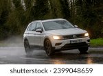 Small photo of Milton Keynes,Bucks,UK - Dec 9th 2023: 2017 white diesel engine Volkswagen Tiguan car driving on a wet road, in the rain with headlights on
