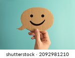 Female hand holding a smiley face speech bubble paper cute against green background.
