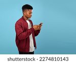 Small photo of Portrait of happy African American man texting with phone. Young beardless man using smartphone against blue background. Social networking concept, Copy space