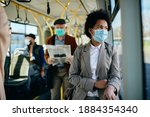 Small photo of Distraught African American businesswoman wearing face mask and looking through a window while commuting to work by bus.