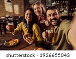 Small photo of Carefree friends taking selfie while drinking beer and eating hamburgers in a bar.