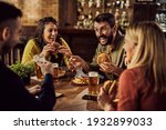 Small photo of Young happy man having fun with is friends while eating hamburgers and drinking beer in a pub.