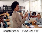 Happy African American professor receives applause from her students while lecturing them in the classroom.
