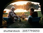 Rear view of man and his nature father having a drink while camping and fishing at sunset. The view is from a tent.