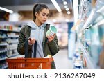 Small photo of Young woman buying diary product and reading food label in grocery store.