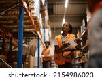 African American female worker going through inventory list while checking stock at distribution warehouse.