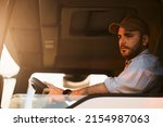 Small photo of Professional truck driver driving in reverse while looking in side view mirror.