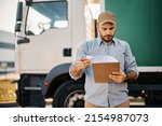 Small photo of Truck driver checking shipment list while standing on parking lot of distribution warehouse.
